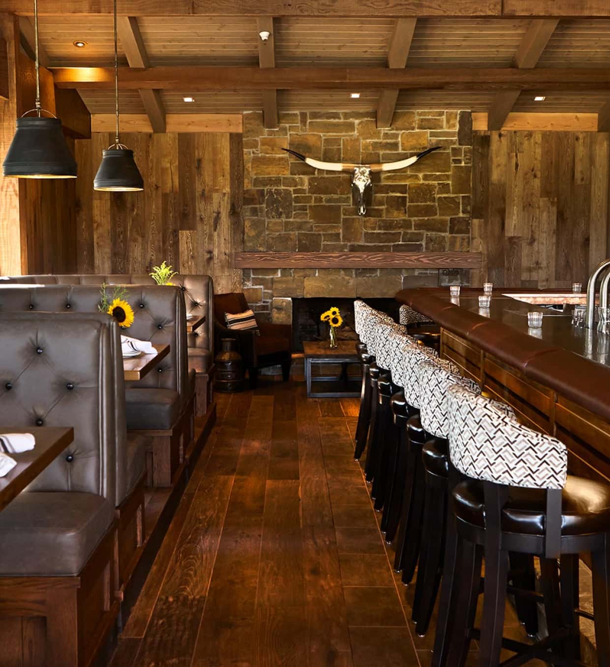 Interior view of 'CORK & FIRE' restaurant showing a rustic dining space with wood paneling, leather seats, black bar stools, and pendant lighting.